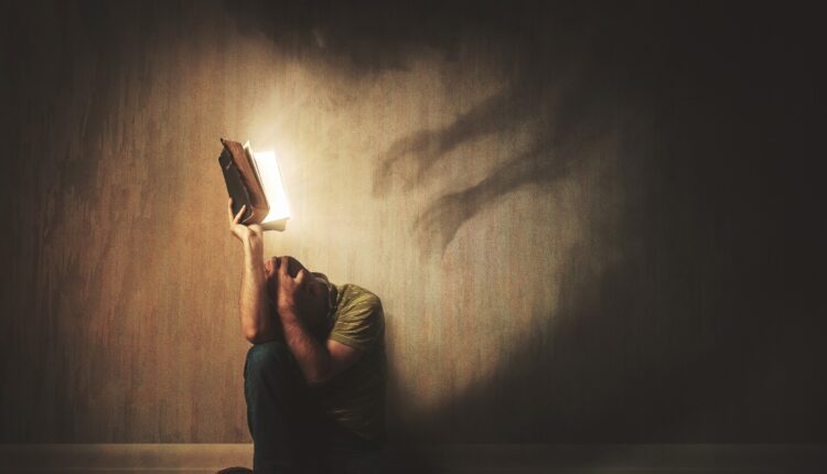 A man holds up a Bible to dark shadows